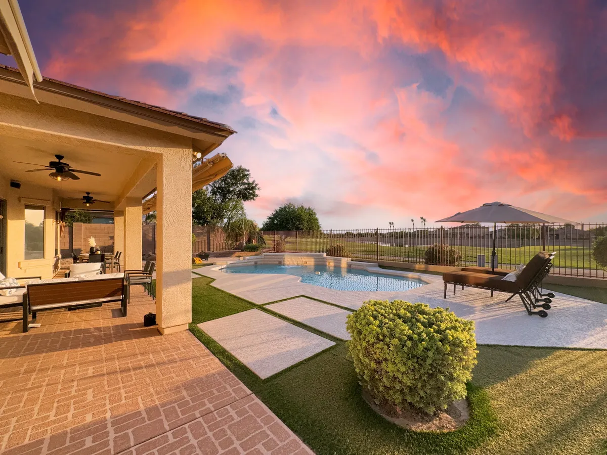 A beautifully landscaped backyard featuring a heated swimming pool, a spacious patio seating area with comfortable furnishings, and lush greenery surrounding the space. The scene suggests a tranquil environment perfect for both relaxation and entertaining, with ample room for outdoor dining or taking a break from work.