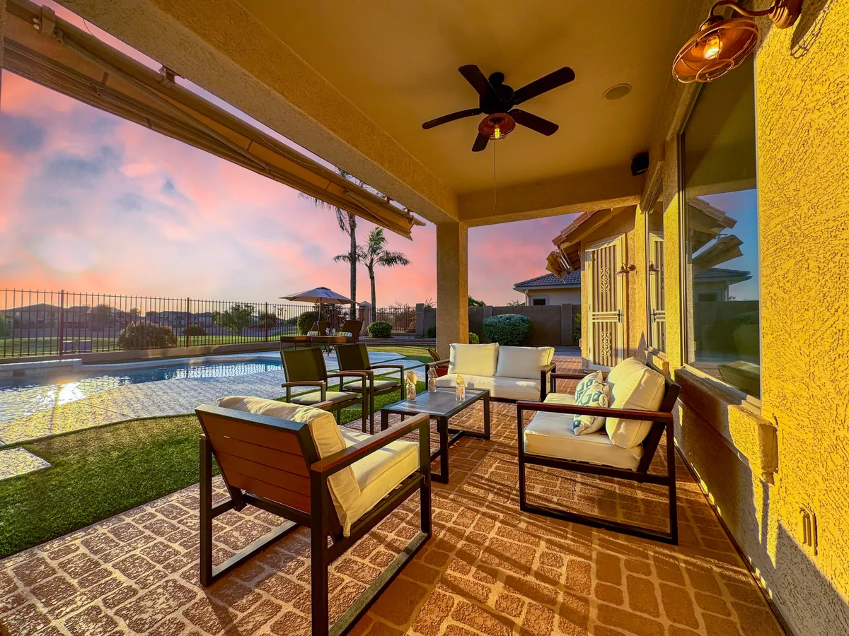 An outdoor seating area overlooking a sparkling pool, adorned with decorative pillows and surrounded by a serene sunset sky. The space invites morning coffee, casual gatherings, or evening relaxation under the stars, creating a seamless connection between work and leisure.
