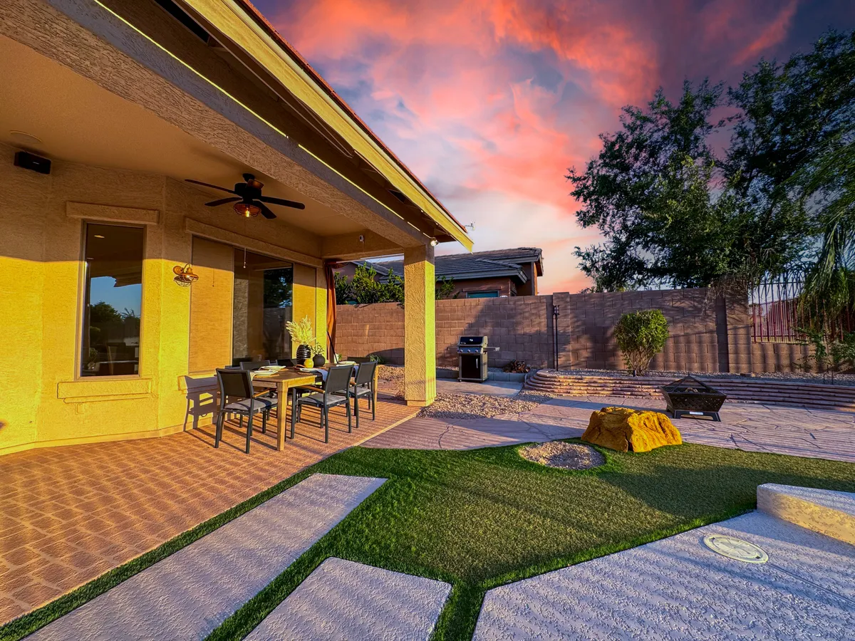 Set in a backyard at sunset, this image features an outdoor dining table with chairs and a barbecue grill, surrounded by lush greenery and a colorful evening sky. The scene evokes moments of outdoor dining, barbecuing, and relaxing together as a family.